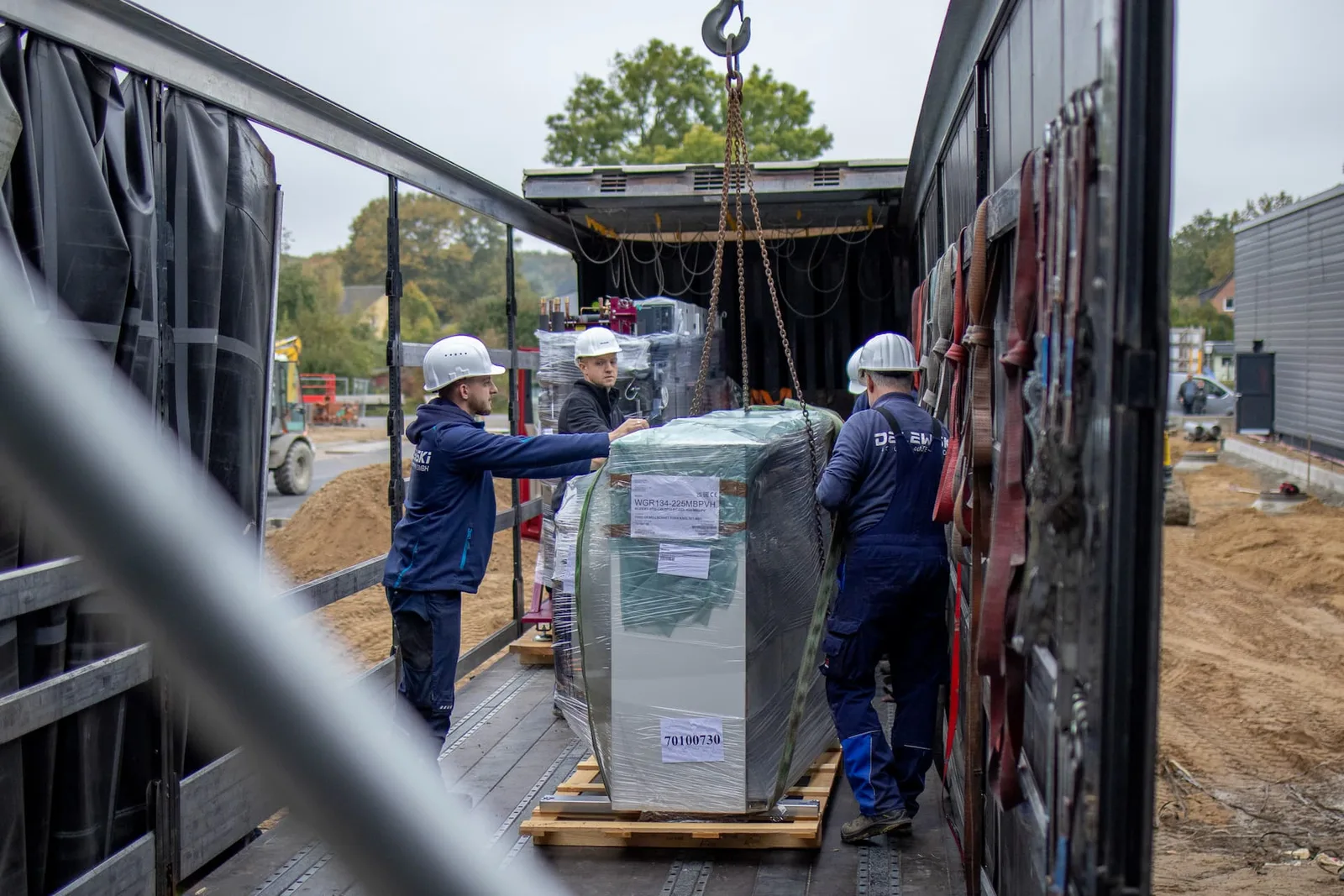 Ein verpacktes Gerät wird am Kranhaken vom Lastwagen gehoben
