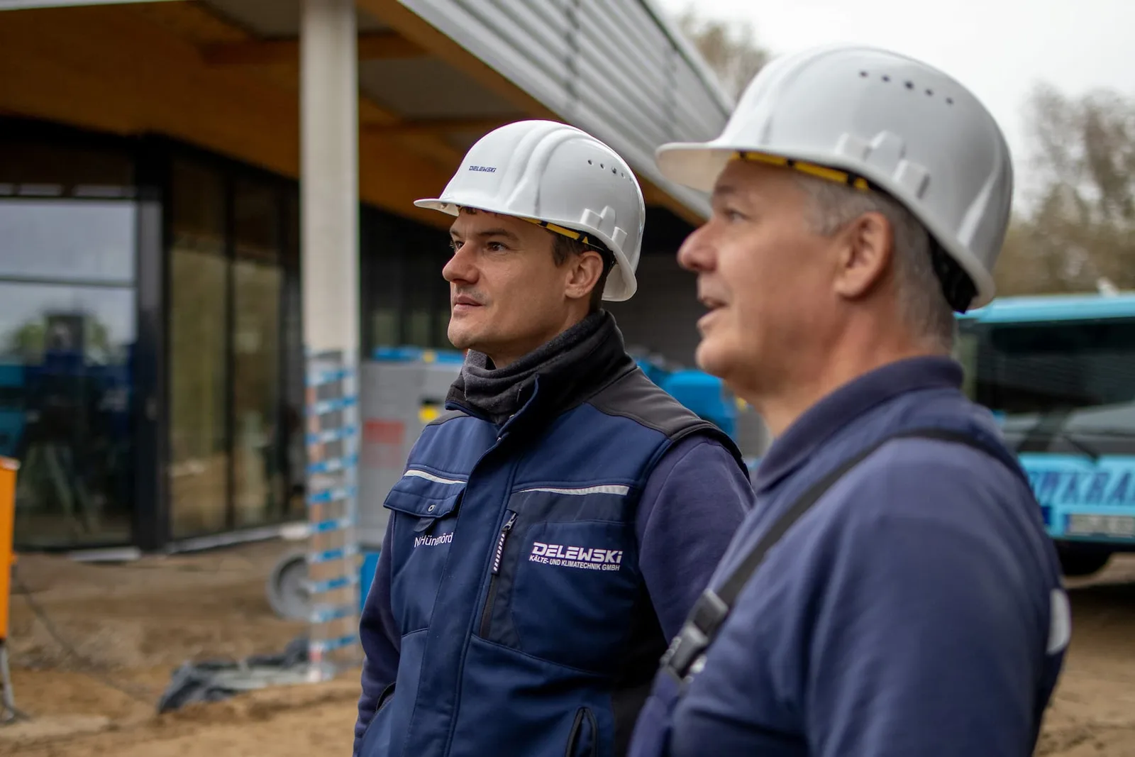 Zwei Monteure mit weißen Helmen blicken über die Baustelle
