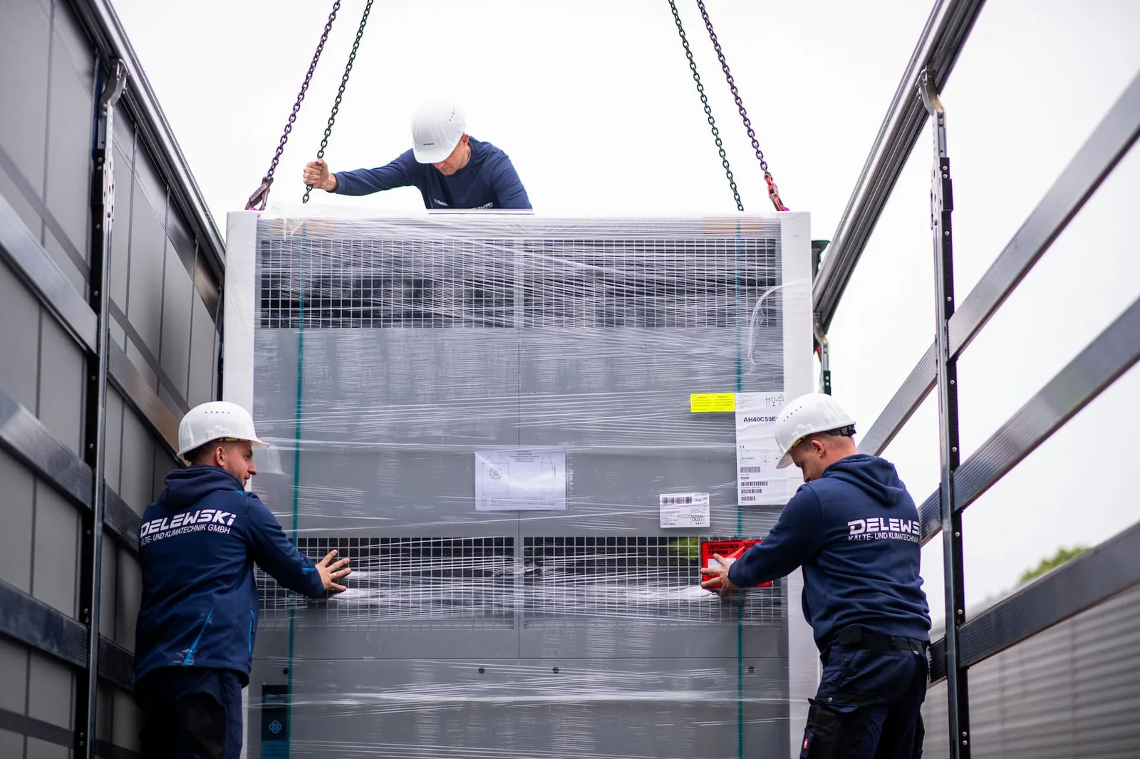 Ein großes, in Folie verpacktes Gerät hängt an Ketten über der Ladefläche