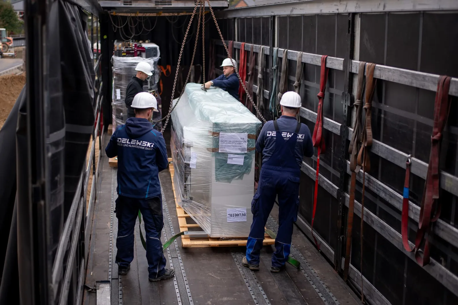 Monteure mit Helmen auf der Ladefläche neben einem verpackten Gerät