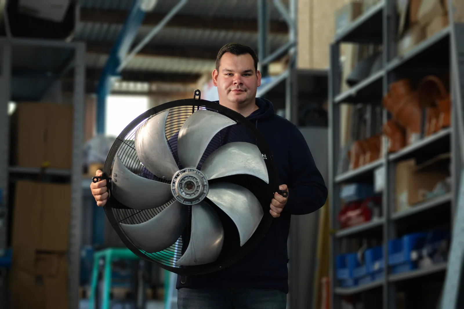 Ein Kollege hält ein großes Ventilatorrad im Lager vor sich