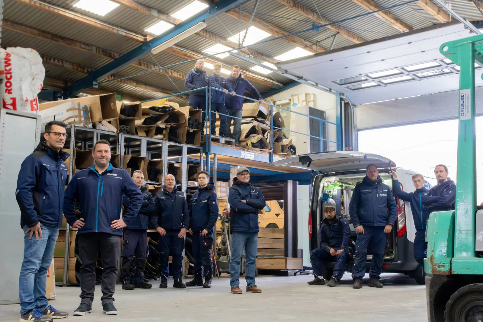 Das Team steht in der Lagerhalle vor einem Transporter und Regalen